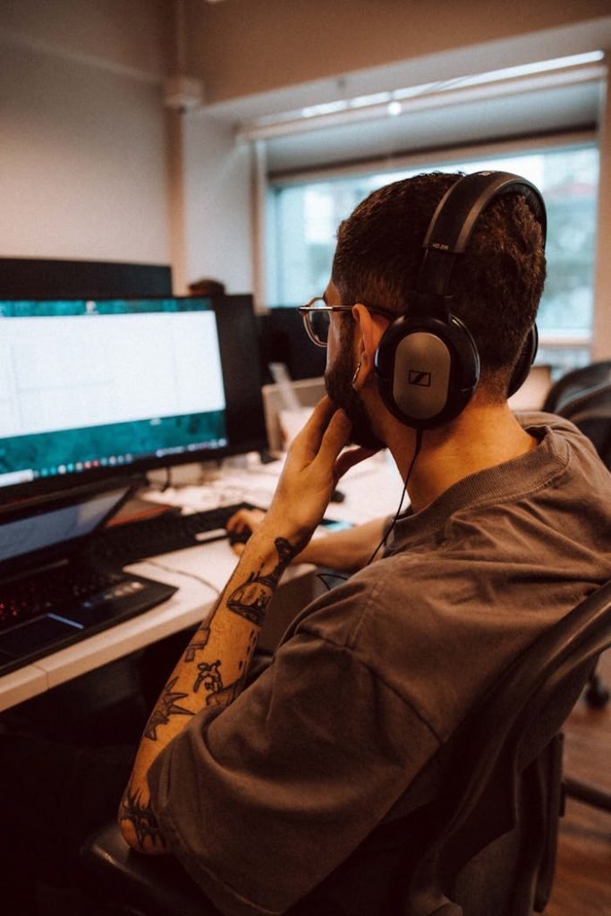 Young adult man focused on computer screen while wearing headphones in an office setting.