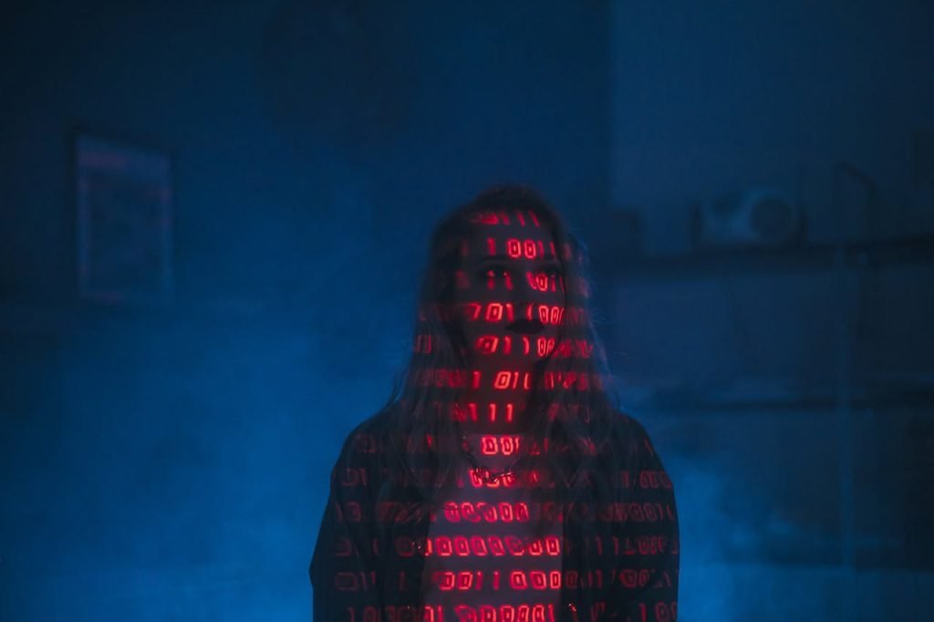 A mysterious silhouette with red binary code projected over the face, set against a dark, moody background.